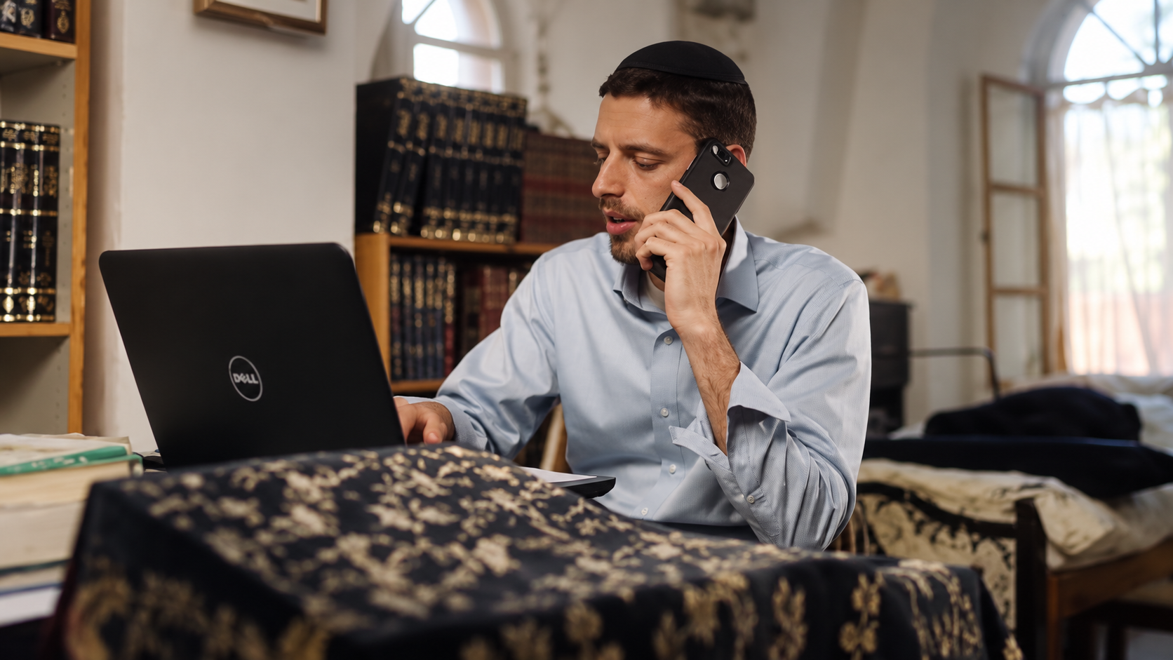 בחור עובד עם מחשב נייד ומדבר בטלפון בבית המדרש
